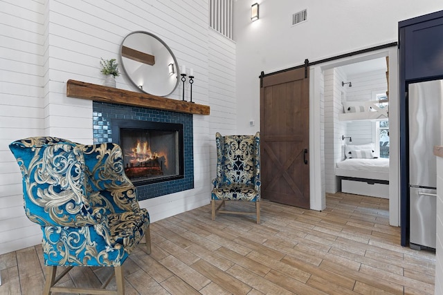 living area with light wood-style floors, visible vents, a tiled fireplace, and a barn door