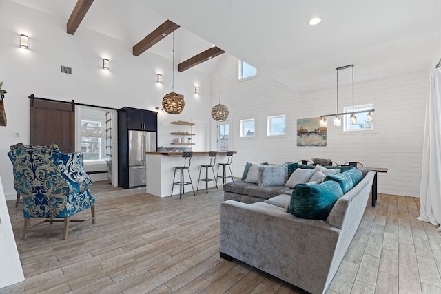 living area featuring a barn door, visible vents, light wood-style floors, high vaulted ceiling, and beam ceiling