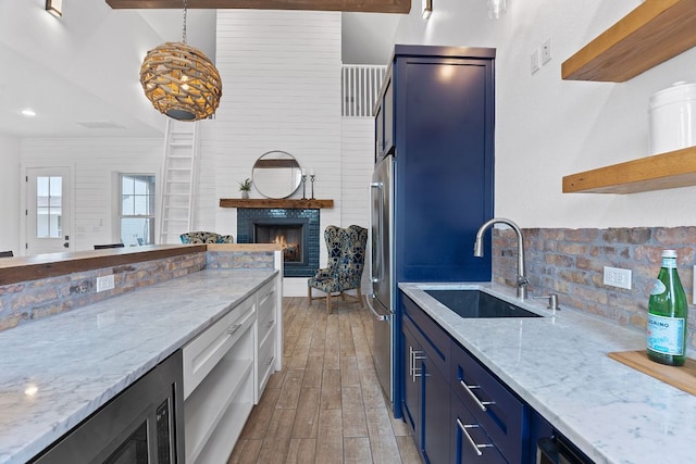 kitchen featuring light wood finished floors, blue cabinetry, a fireplace, open shelves, and a sink