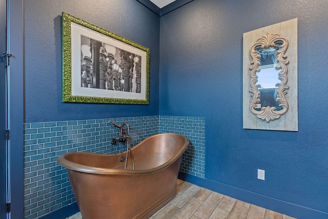 full bath featuring tile walls, a textured wall, a freestanding bath, wainscoting, and wood finished floors