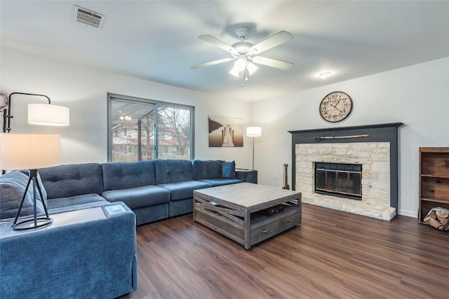 living area with ceiling fan, a stone fireplace, dark wood-style flooring, and visible vents