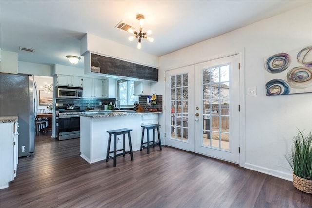 kitchen featuring decorative backsplash, appliances with stainless steel finishes, dark wood-style flooring, a peninsula, and an inviting chandelier