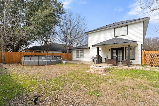 rear view of property featuring a patio, a fenced backyard, a fire pit, french doors, and a fenced in pool