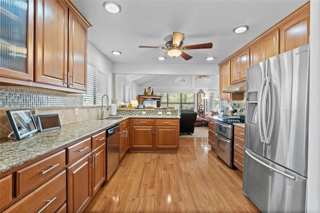 kitchen with light stone counters, under cabinet range hood, stainless steel appliances, a peninsula, and a sink