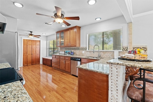 kitchen featuring brown cabinets, appliances with stainless steel finishes, a sink, a peninsula, and a kitchen bar