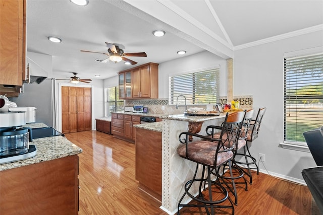 kitchen with light stone counters, a peninsula, a kitchen breakfast bar, tasteful backsplash, and brown cabinetry