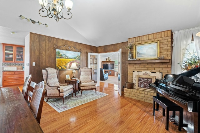 living area with a notable chandelier, wooden walls, a brick fireplace, and light wood-style floors