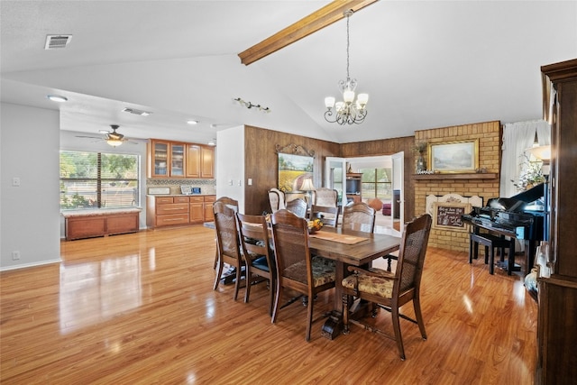 dining space with ceiling fan with notable chandelier, visible vents, light wood-type flooring, a brick fireplace, and beamed ceiling