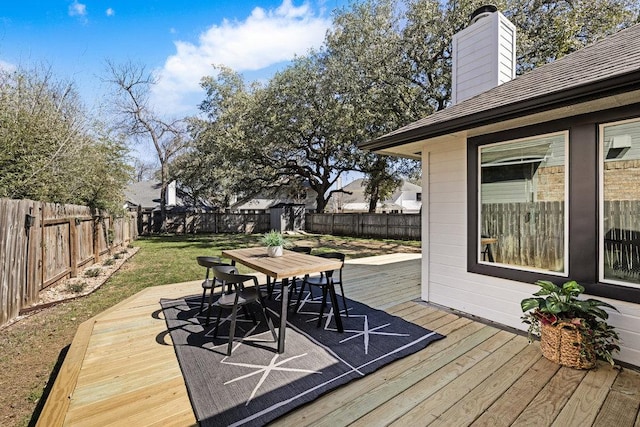 wooden deck featuring an outbuilding, outdoor dining area, a fenced backyard, and a lawn