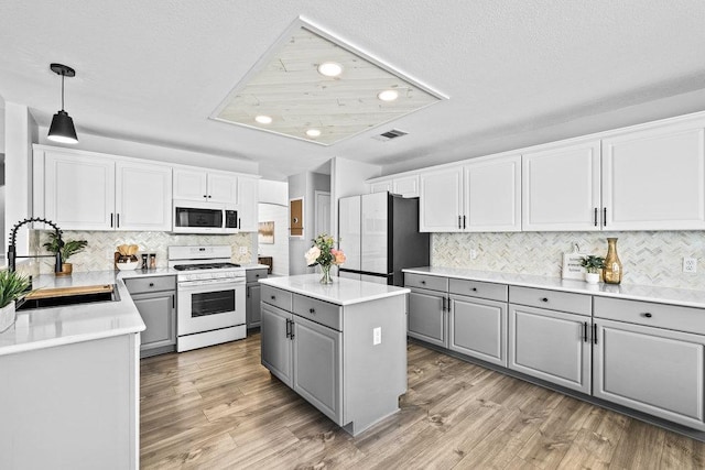 kitchen featuring white appliances, light wood finished floors, a sink, and gray cabinetry