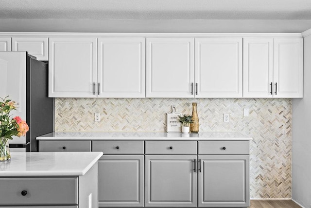 kitchen with white cabinets, light countertops, gray cabinets, freestanding refrigerator, and decorative backsplash