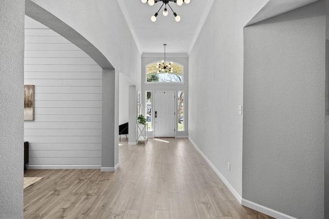 foyer featuring arched walkways, crown molding, wood finished floors, a chandelier, and baseboards