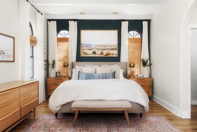 bedroom with baseboards, arched walkways, and wood finished floors