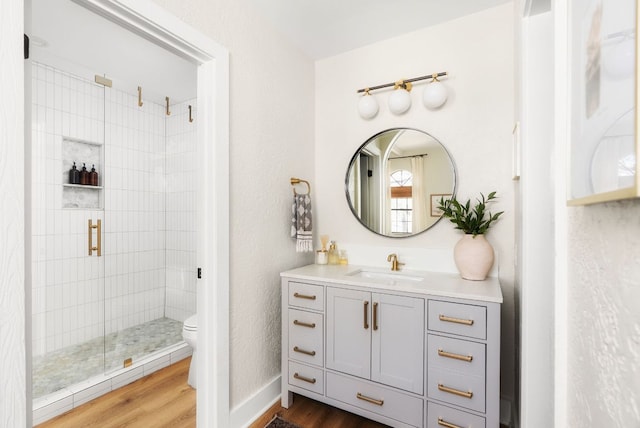 bathroom featuring toilet, a stall shower, wood finished floors, and vanity