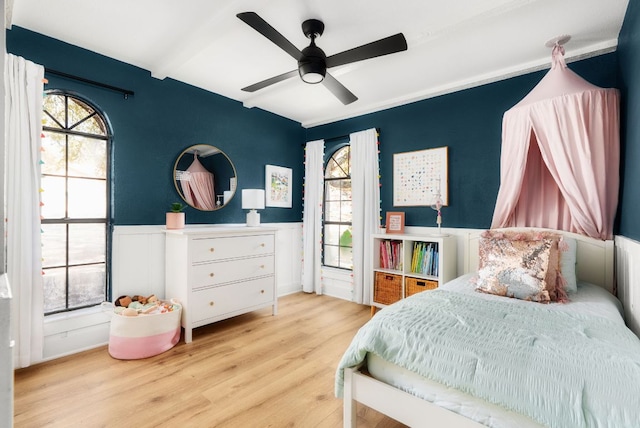 bedroom featuring a wainscoted wall, multiple windows, ceiling fan, and wood finished floors