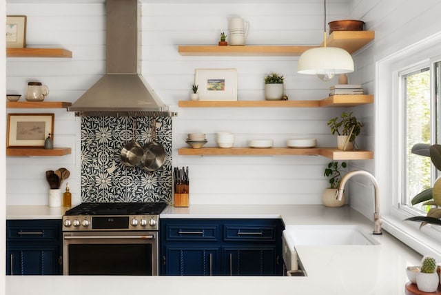 kitchen featuring open shelves, stainless steel gas range, wall chimney exhaust hood, and blue cabinets