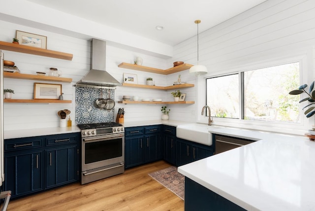 kitchen with open shelves, stainless steel appliances, a sink, blue cabinets, and wall chimney exhaust hood