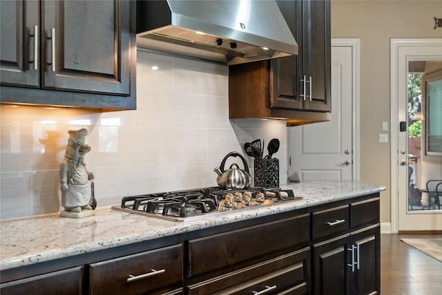 2717 Rain Song Dr, Leander, TX 78641 - kitchen with ventilation hood, backsplash, light stone countertops, dark brown cabinetry, and stainless steel gas cooktop