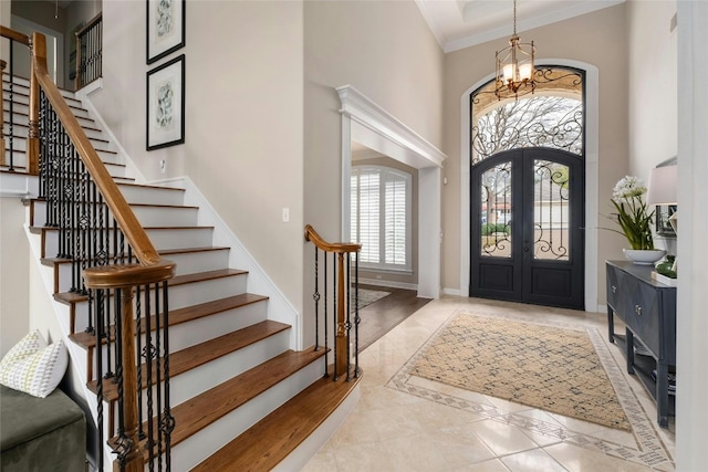 foyer with french doors, a notable chandelier, crown molding, a towering ceiling, and baseboards