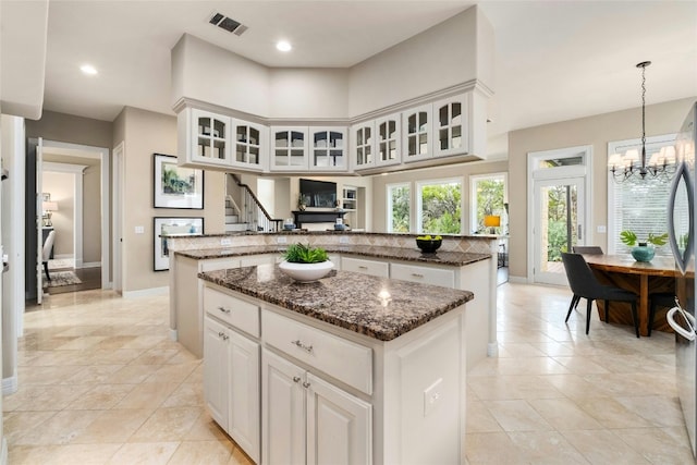 kitchen with a kitchen island, visible vents, dark stone countertops, glass insert cabinets, and an inviting chandelier