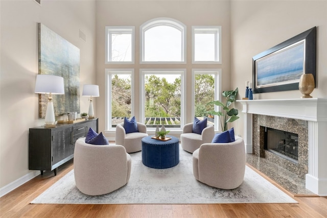 living area featuring a high ceiling, a premium fireplace, baseboards, and wood finished floors