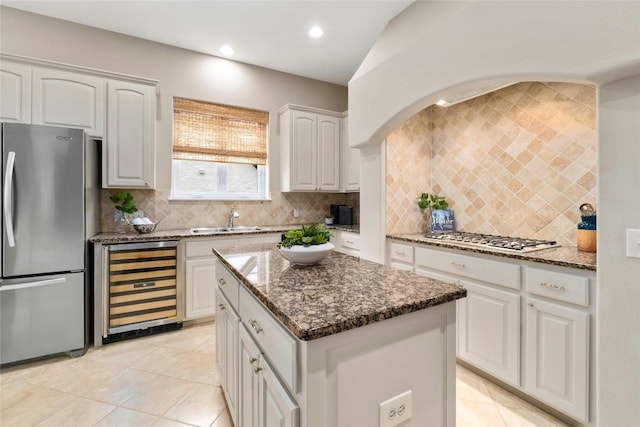 kitchen with beverage cooler, a kitchen island, appliances with stainless steel finishes, dark stone countertops, and a sink