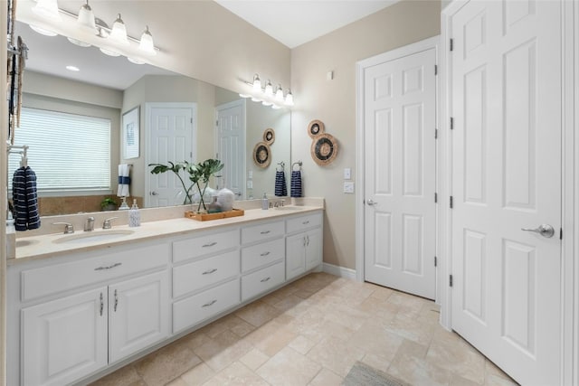 bathroom with stone finish floor, a sink, baseboards, and double vanity