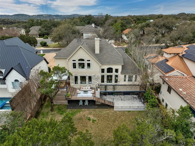 rear view of property featuring a yard, a chimney, a residential view, stone siding, and a wooden deck