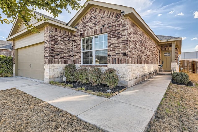 view of front of home featuring driveway, stone siding, an attached garage, fence, and brick siding