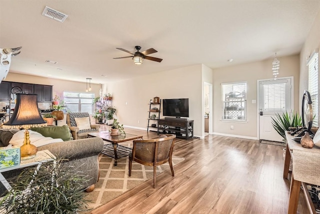 living room with light wood-type flooring, a healthy amount of sunlight, visible vents, and baseboards