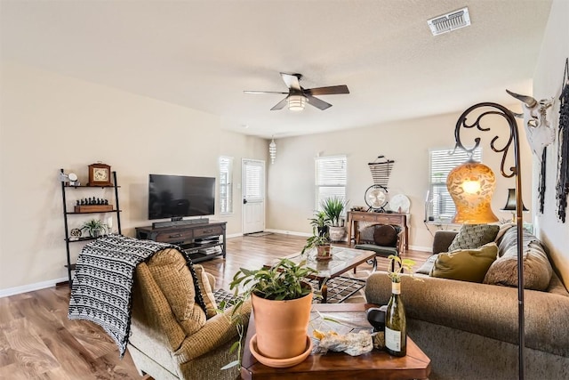 living area featuring baseboards, wood finished floors, visible vents, and a ceiling fan