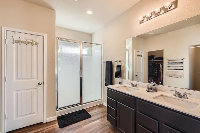 full bathroom featuring double vanity, wood finished floors, a stall shower, and a sink