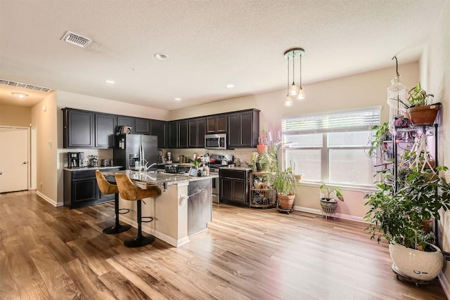 kitchen with light wood finished floors, appliances with stainless steel finishes, visible vents, and a kitchen breakfast bar