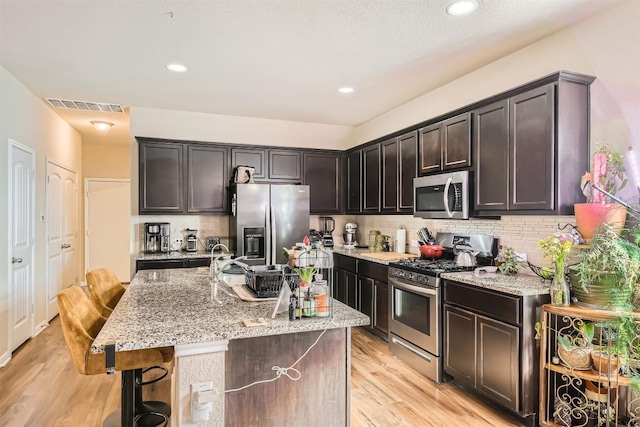 kitchen featuring light stone counters, visible vents, appliances with stainless steel finishes, light wood-type flooring, and backsplash