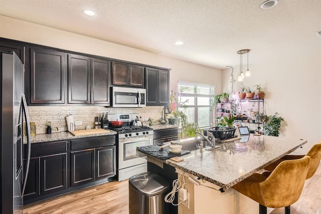 kitchen with light wood-type flooring, light stone countertops, stainless steel appliances, and a sink