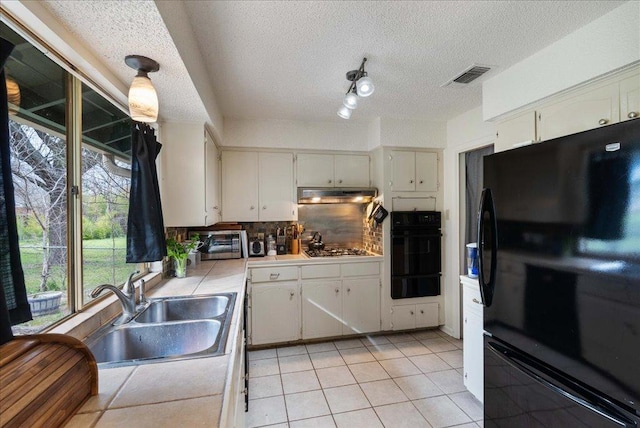 kitchen featuring a warming drawer, tile counters, a sink, under cabinet range hood, and black appliances