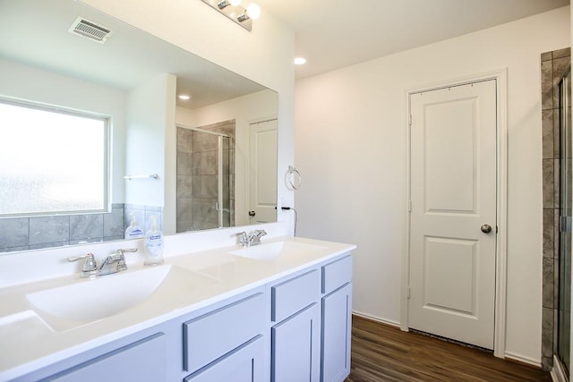 full bathroom with double vanity, a sink, a tile shower, and wood finished floors