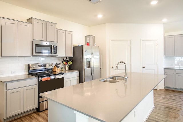 kitchen featuring stainless steel appliances, gray cabinets, a sink, an island with sink, and wood finished floors