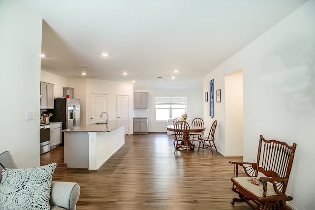 kitchen with dark wood-style floors, stainless steel appliances, gray cabinetry, a kitchen island with sink, and a sink