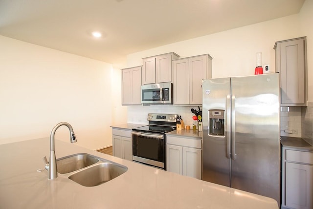 kitchen featuring stainless steel appliances, tasteful backsplash, light countertops, gray cabinetry, and a sink