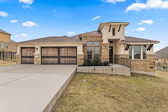 prairie-style home featuring an attached garage, fence, stone siding, concrete driveway, and stucco siding