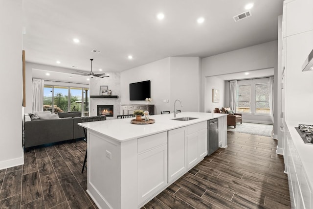 kitchen featuring a large fireplace, a sink, visible vents, white cabinets, and dark wood-style floors