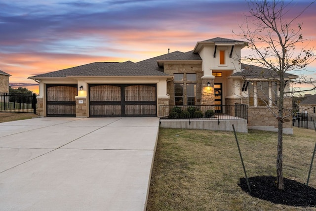 prairie-style house featuring a garage, stone siding, fence, and driveway