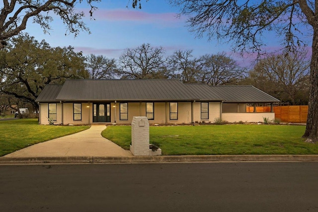 view of front of house with metal roof, a front lawn, fence, and brick siding