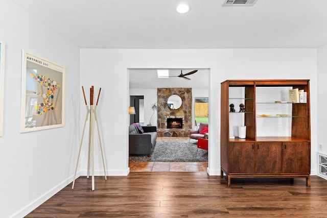 foyer entrance with a stone fireplace, wood finished floors, visible vents, a ceiling fan, and baseboards