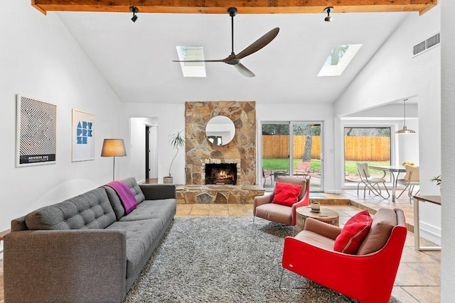 living area featuring a skylight, visible vents, ceiling fan, a stone fireplace, and beam ceiling