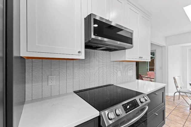 kitchen with light tile patterned floors, appliances with stainless steel finishes, white cabinets, and backsplash