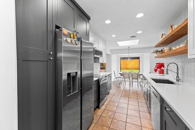 kitchen featuring a skylight, open shelves, backsplash, appliances with stainless steel finishes, and a sink