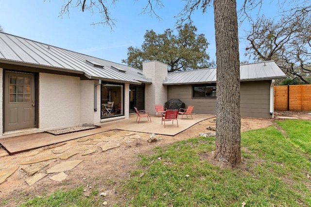 rear view of house featuring metal roof, a patio, a chimney, and fence