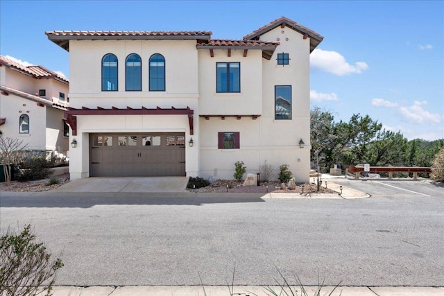 mediterranean / spanish-style home featuring driveway, an attached garage, a tiled roof, and stucco siding